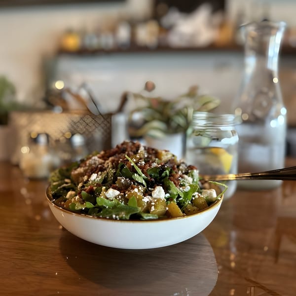 A fresh salad with greens, feta, and nuts in a white bowl on a wooden table.