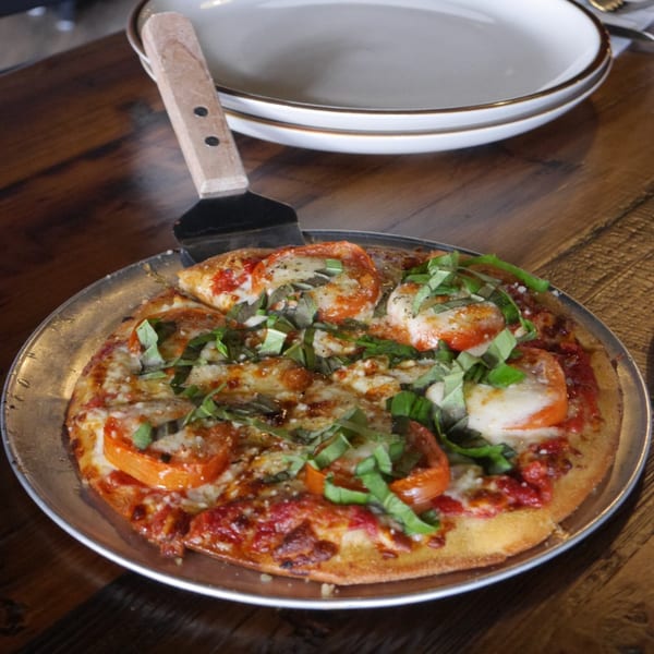 A freshly baked Underground Pizza with tomatoes, mozzarella, and basil, served on a metal pan.