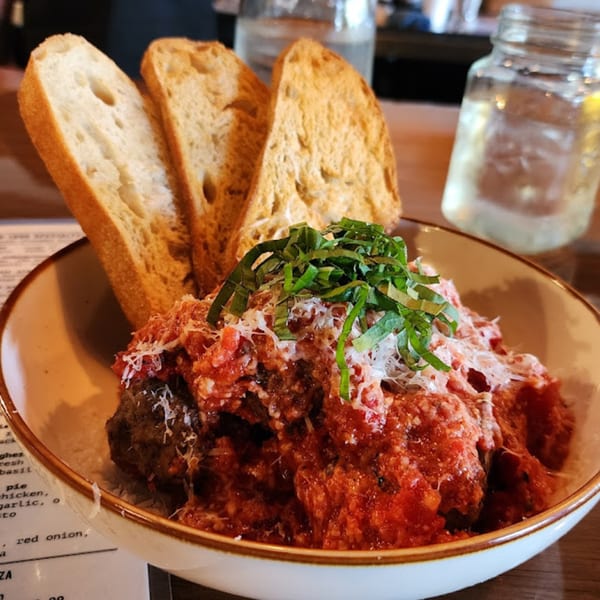 Meatballs in red sauce topped with cheese and basil, served with three slices of bread.