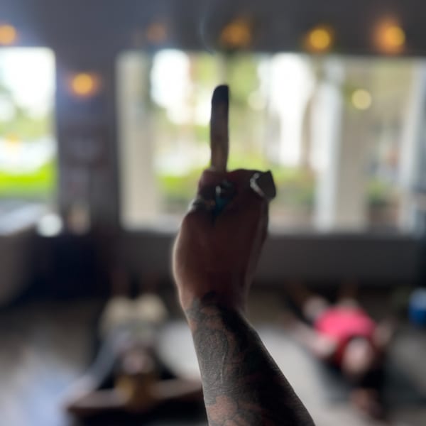 Tattooed hand raises a dark bottle in a softly blurred, warmly lit restaurant interior.