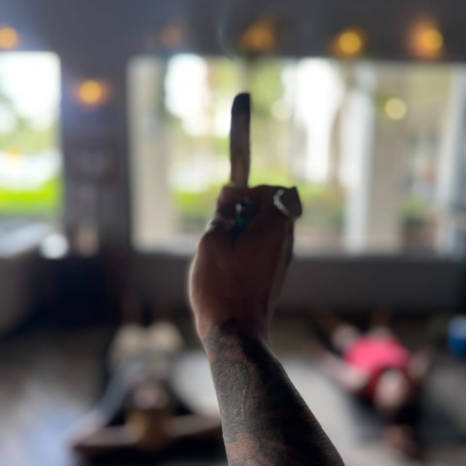 Tattooed hand raises a dark bottle in a softly blurred, warmly lit restaurant interior.